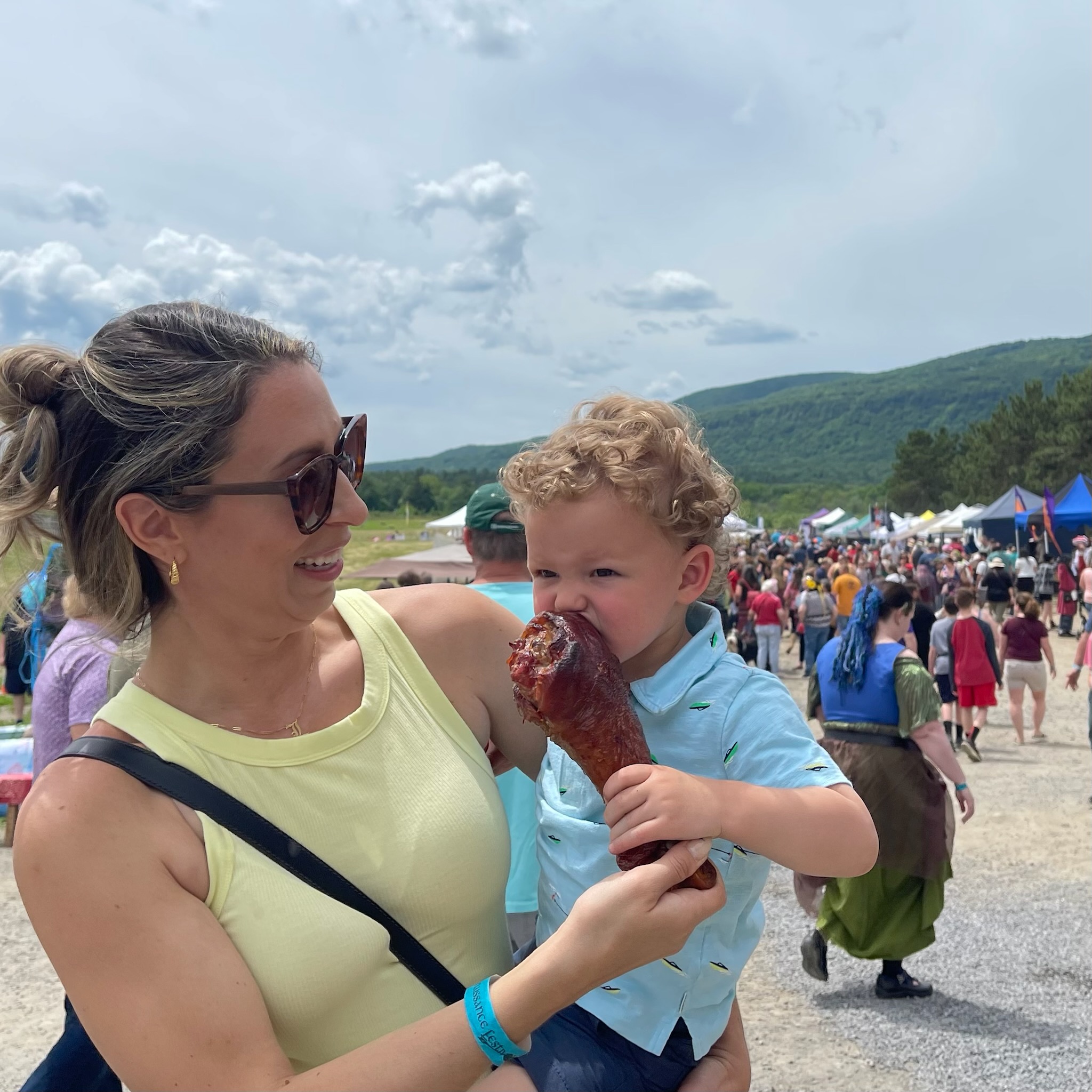 Small child eating a large turkey leg while his mother holds him
